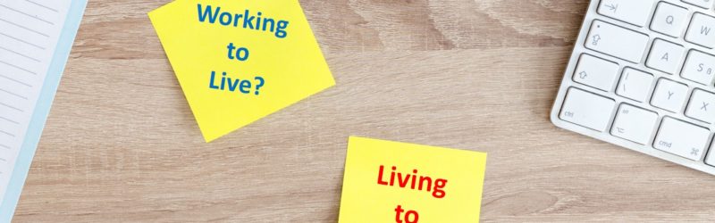 image of a laptop key board and post note on a table reading - Working to Live, Living to Work