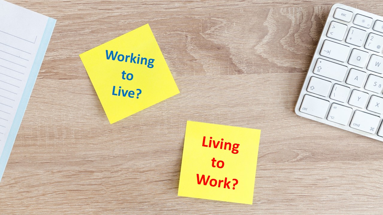 image of a laptop key board and post note on a table reading - Working to Live, Living to Work