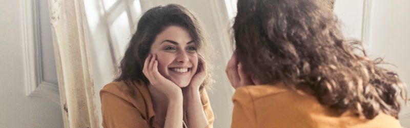 Woman looking at the mirror and smiling happily - No matter what the world says, its ok to live your life